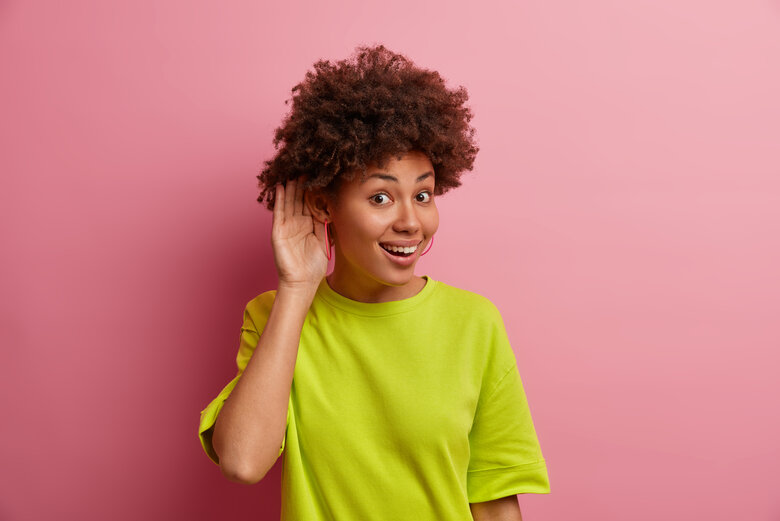 Une femme porte la main à son oreille, faisant comme si elle voulait mieux entendre