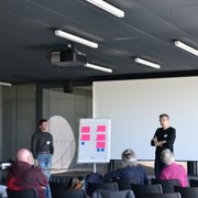 Un homme se tient sur une estrade, à proximité d'un poster avec des post-it