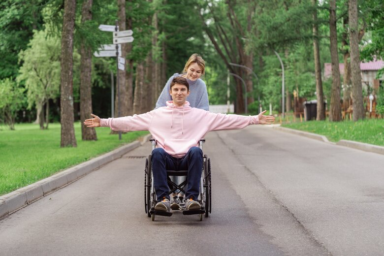 Homme en chaise roulante poussé par une femme