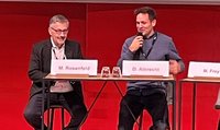 Martin D. Rosenfeld und Daniel Albrecht sitzen am Podium. Daniel Albrecht hält ein Mikrofon in der Hand.