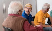 Extrait d'un groupe de parole. Une personne au premier plan tourne le dos à la caméra et est en conversation avec la personne à côté. La troisième personne est tournée vers une autre personne en dehors du cadre.