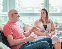 [Bitte in "Französich" uebersetzen:] Ein Mann und eine Frau sitzen auf einem Sofa. Der Mann spricht und die Frau hört zu.