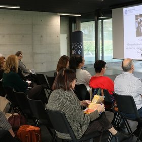 Conférence Lavigny Une femme se tient derrière un pupitre, des personnes assises face à elle l'écoutent