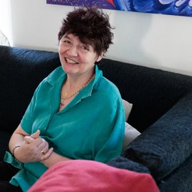 Sonia F. T. Une femme vêtue d'une blouse bleue assise sur un canapé