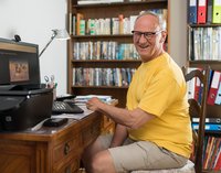 Ein Mann sitzt vor dem Computer und lächelt in die Kamera