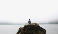 Ein Mensch sitzt auf einem Felsen in einem Nebelmeer.