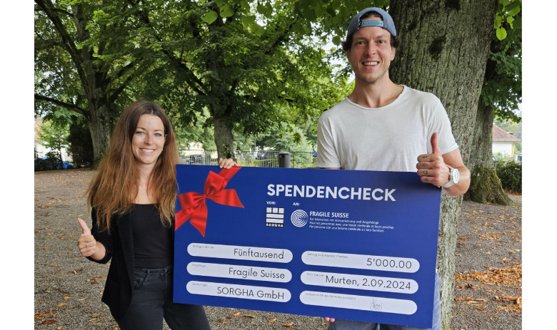 Zwei Personen posieren mit einem grossen blauen Spendencheck: links Jana Bauer, rechts Kevin Lötscher. Sie lächeln und halten den Daumen hoch.