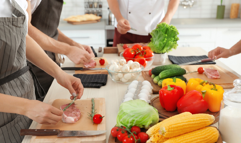 Kochen mit freude Bunte Zutaten liegen auf einem Tisch. Drei paar Hände sind dabei, sie zu verarbeiten.