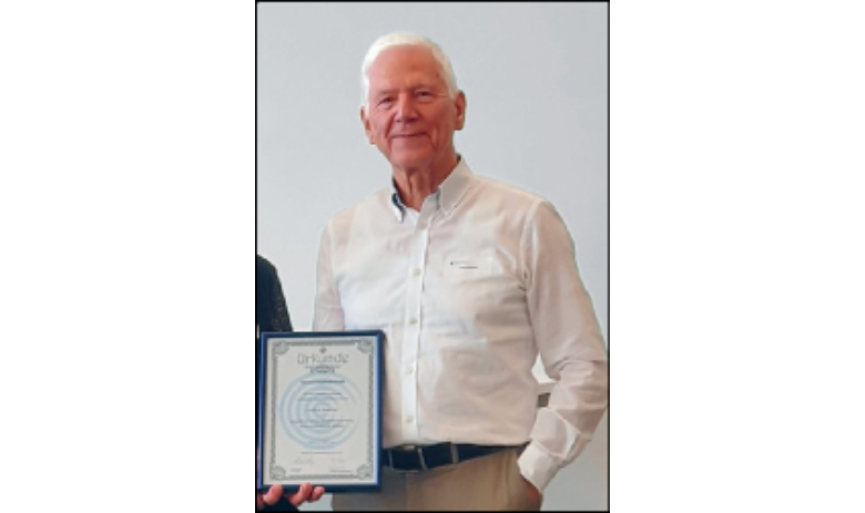 Prof. Dr. Ulrich W. Buettner Portraitfoto eines Mannes in einem weissen Hemd. Er hält ein Diplom in der Hand.