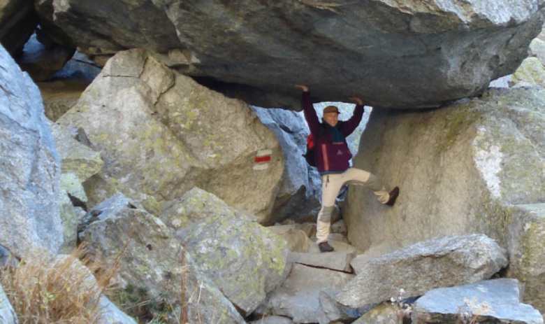 Eine Person steht unter einem Felsen auf einem Wanderweg. Die Arme nach oben gestemmt, als ob sie den Felsen hochhalten würde.