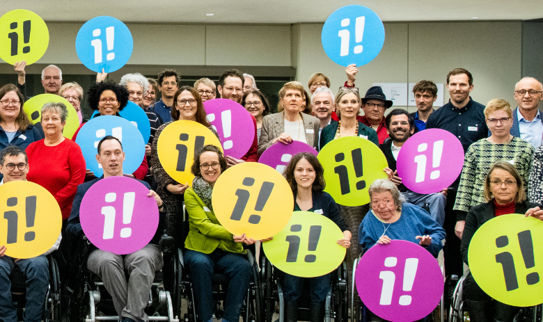 Gruppenfoto. Zahlreiche Personen halten bunte Logos der Inklusions-Initiative hoch.