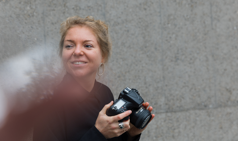 Künstlerisches Foto von Damaris B. Sie lächelt mit dem Blick nach links und mit der Fotokamera in der Hand.
