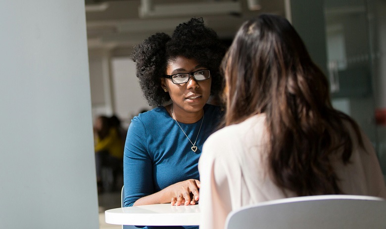 Zwei Personen gegenüber an einem Tisch in einem Beratungsgespräch.