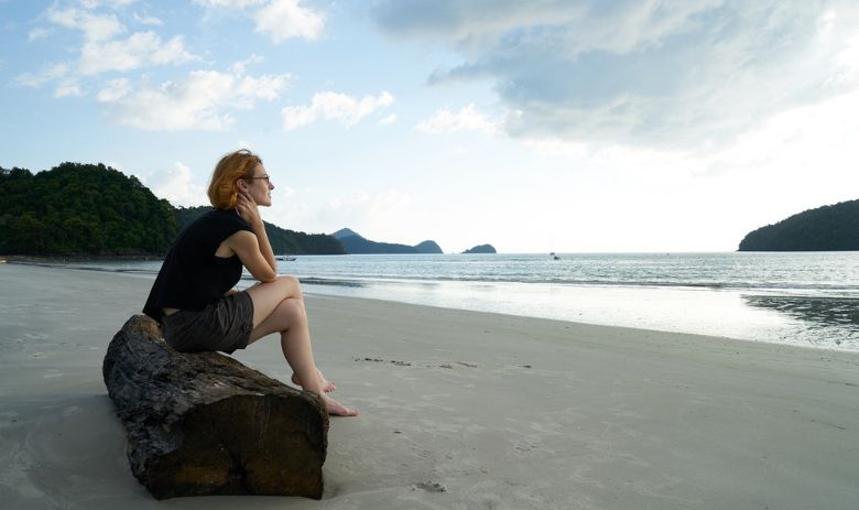 Eine Frau sitzt alleine am Strand.