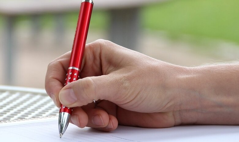 Une main tient un stylo et écrit sur une feuille