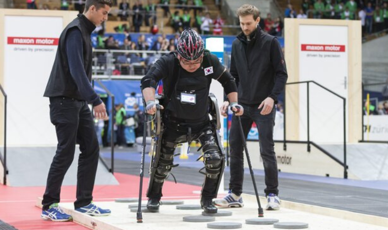 Drei Personen, in der Mitte Mann mit Gehhilfe, der an einer Cybathlon Disziplin teilnimmt 