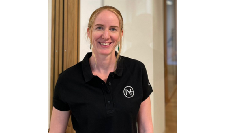 Profilfoto einer Frau mit hellen Haaren. Sie trägt ein schwarzes Poloshirt mit einem Logo darauf und lächelt in die Kamera.